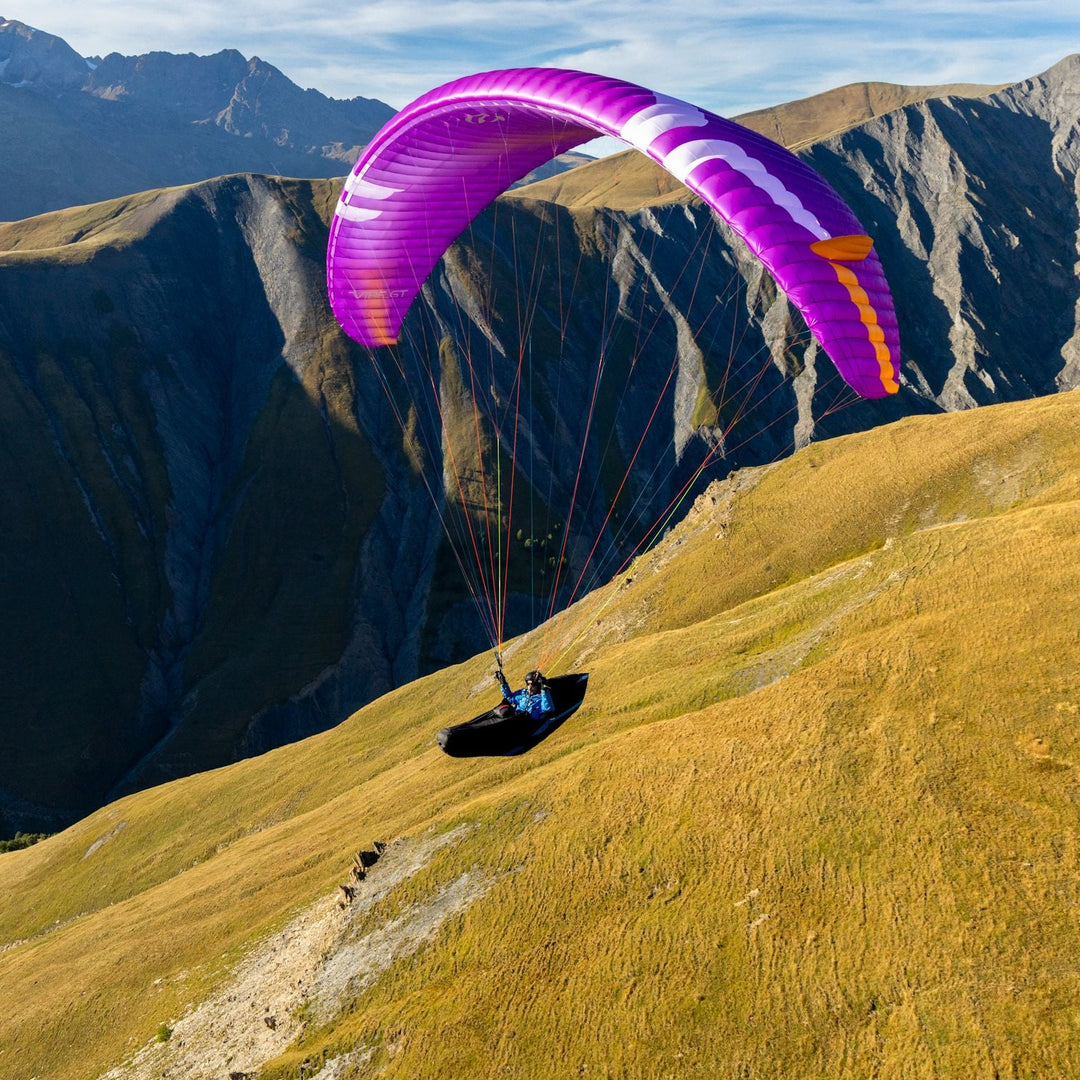 Person paragliding on a grassy hill with mountains in the background